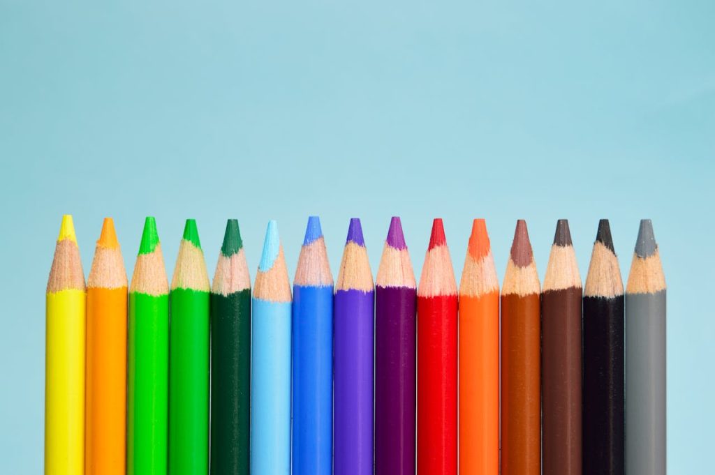 A row of vibrant colored pencils lined up on a soft blue background, showcasing a spectrum of colors.