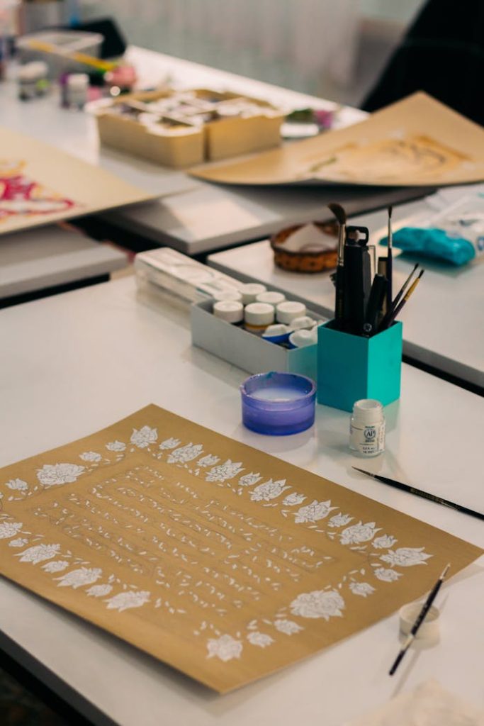 Art supplies arranged on a table with paintings, brushes, and decorative paper.
