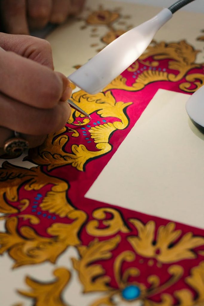 Close-up of hands painting an ornate gold and red design. Artistic craftsmanship.